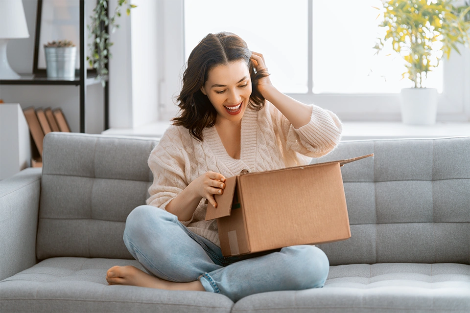 Woman opening up a gifted box and smiling on the couch