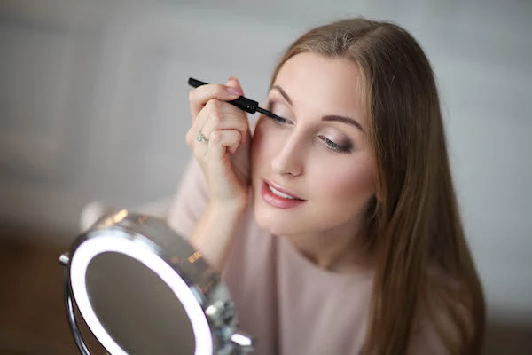 Beauty vlogger doing her makeup in front of a lighted mirror