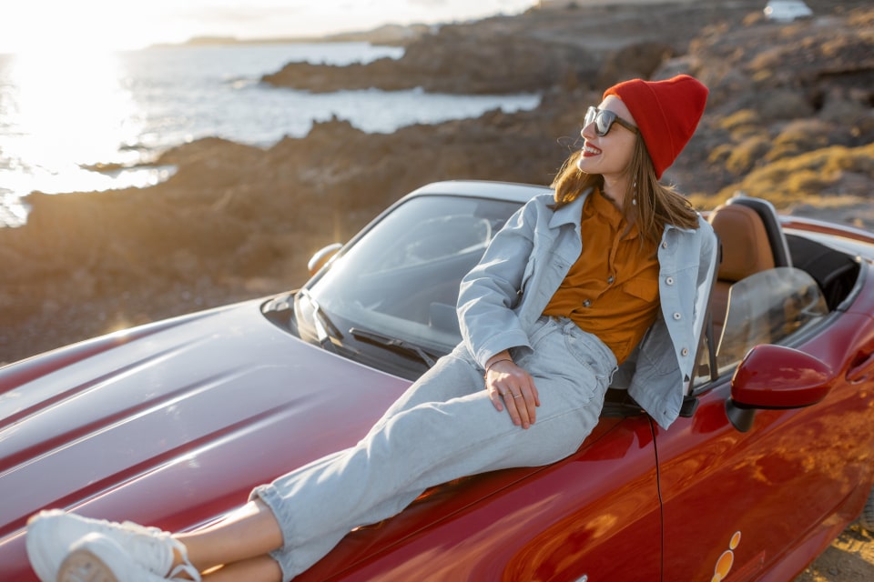 Automotive influencer sitting on a red car by the coast