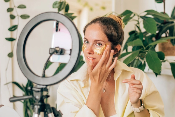 skincare influencer applying a gold product to her face while filming herself
