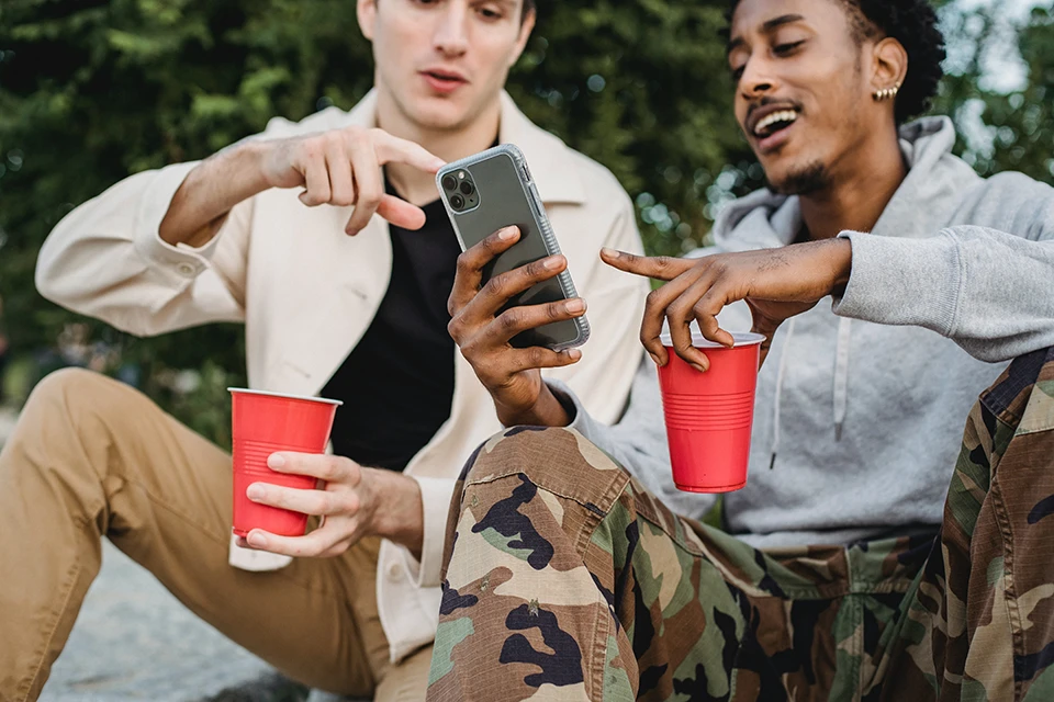 Two men with red cups pointing at a smartphone demonstrating influencer marketing for ecommerce starts with a like-minded audience