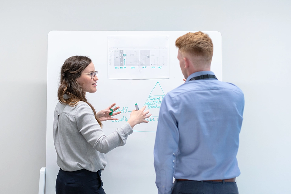 Two coworkers discussing work on a whiteboard showing focusing on data can help with marketing in a recession