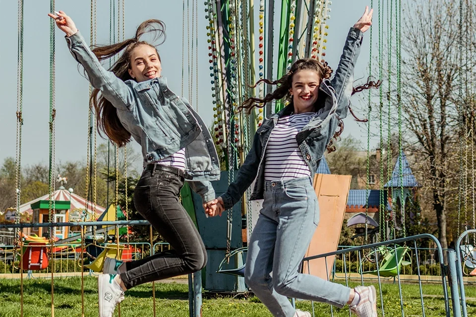 two teenage influencers jumping in the air in front of a carnival swing ride