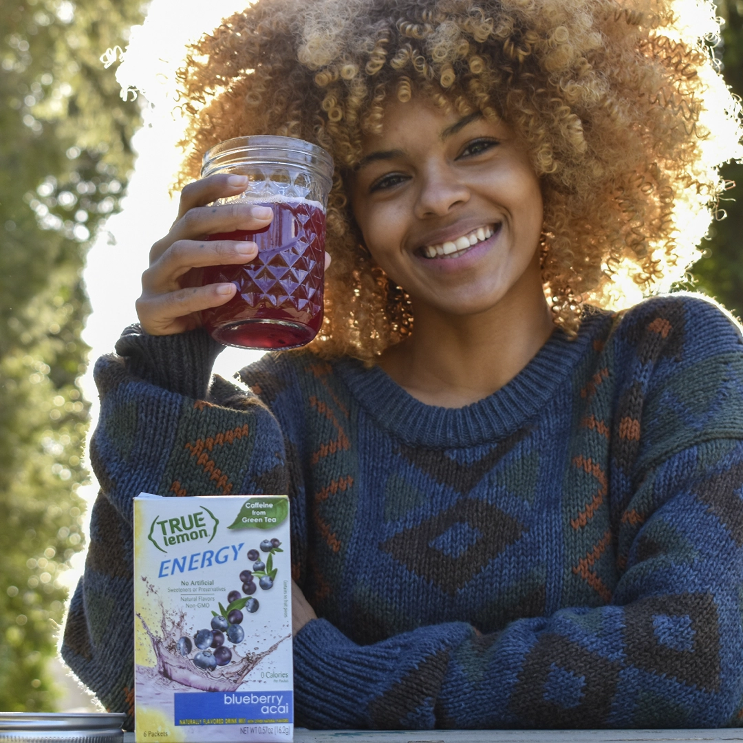 Woman smiling and holding up blueberry True Citrus