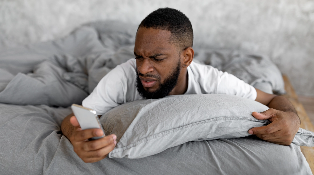 Confused man looking at a smartphone in bed