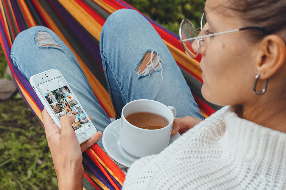 A woman drinking coffee in a hammock browsing Instagram and participating in the Instagram algorithm
