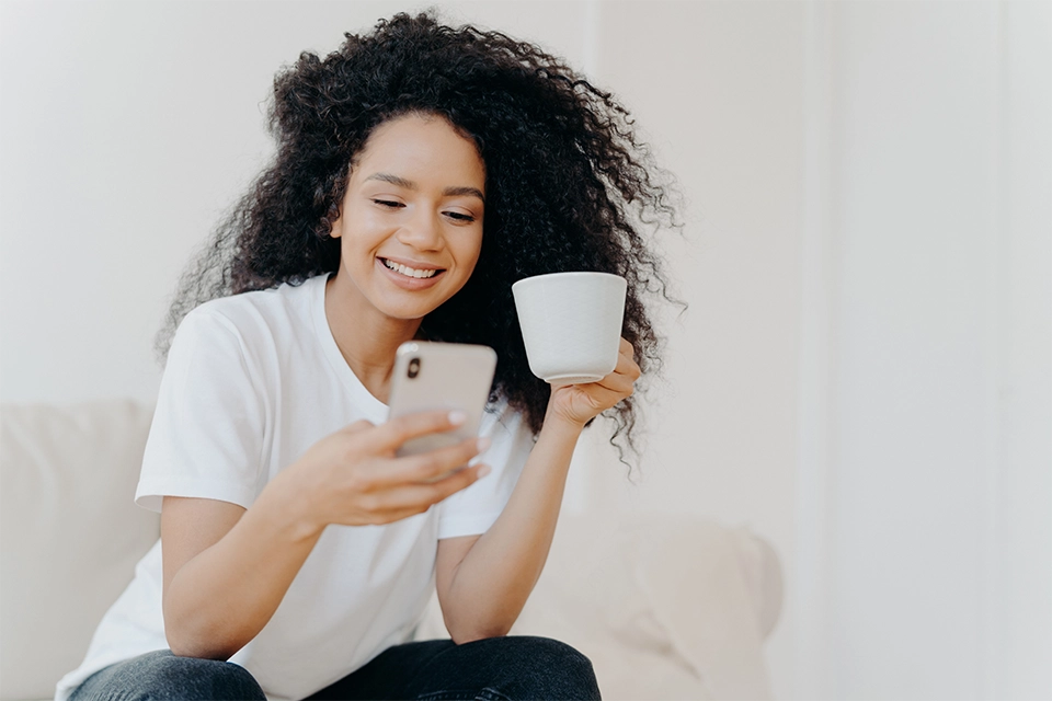 Woman smiling at her phone and holding a mug having received a dynamic payout