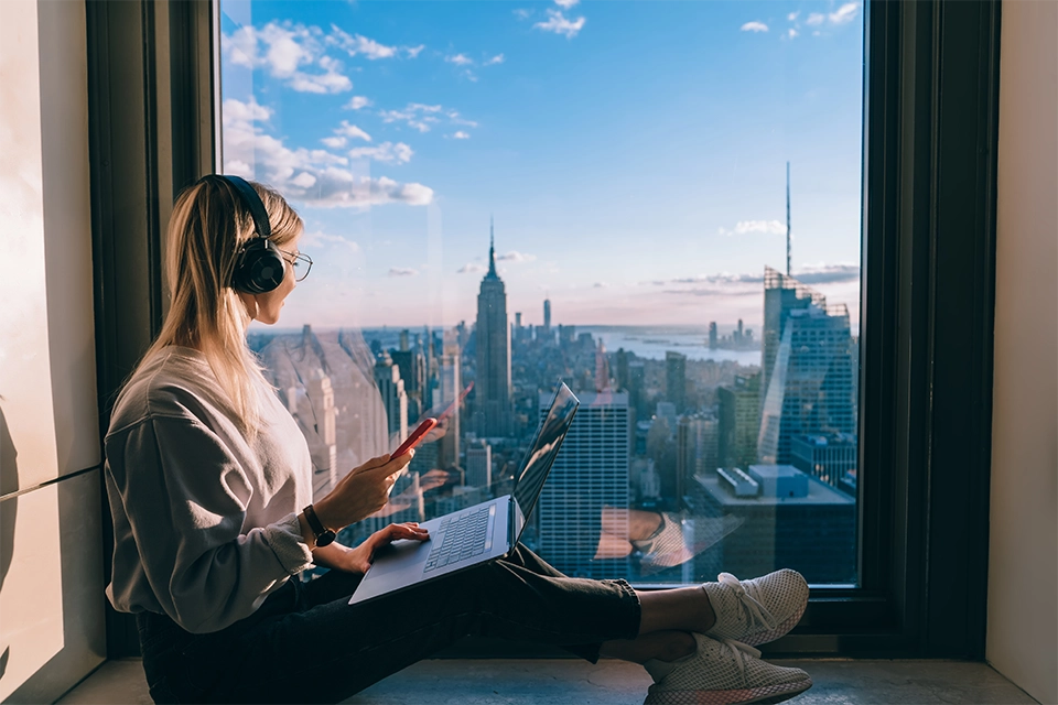 woman in headphones in a window staring out at a cityscape as an example of hotel influencers