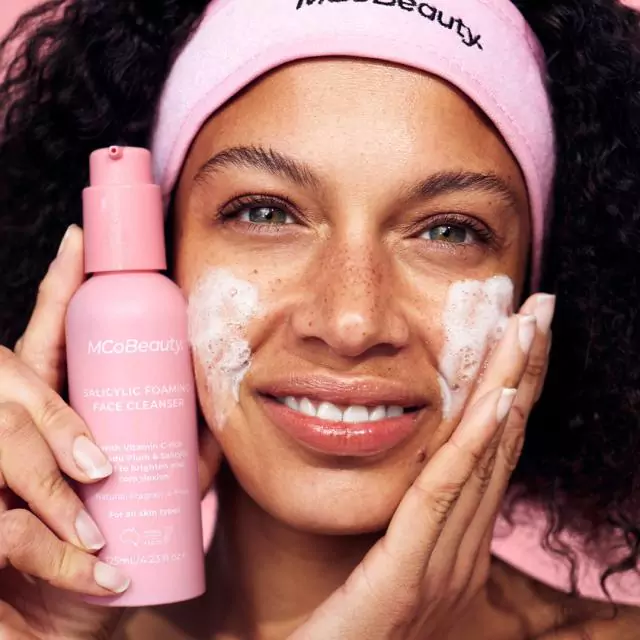Smiling woman holding up and using foaming face cleanser