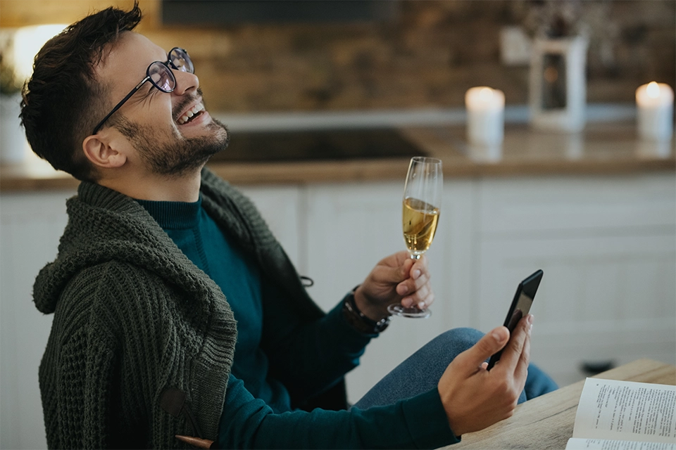 Man with champagne and a phone laughing about his dating app marketing success