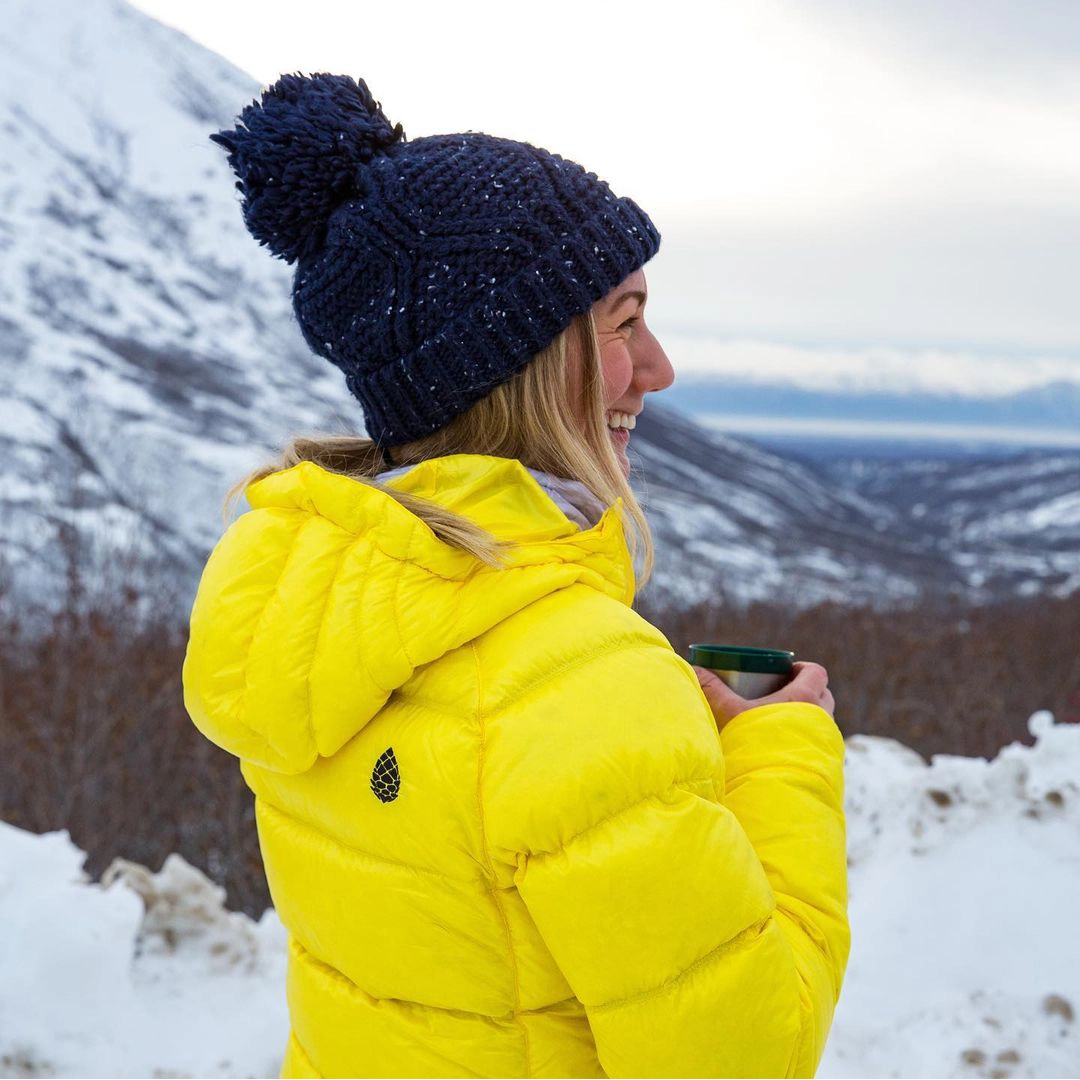 Woman in a yellow jacket and beanie smiling in a snowy environment