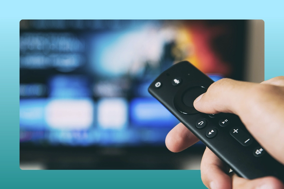 A remote in a hand in front of a TV symbolizing TV show marketing